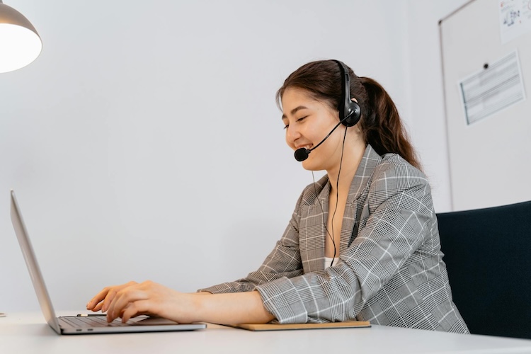 woman typing on laptop while chatting via headset